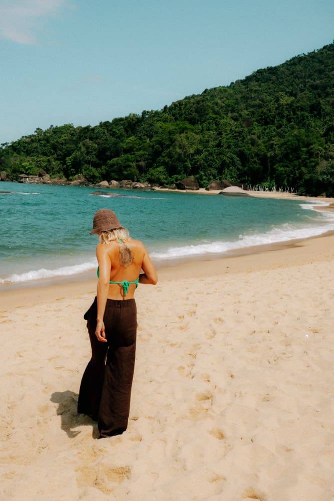 Femme en pantalon noir de dos sur la plage face à la baie, photographie lifestyle au Club Med Rio das Pedras
