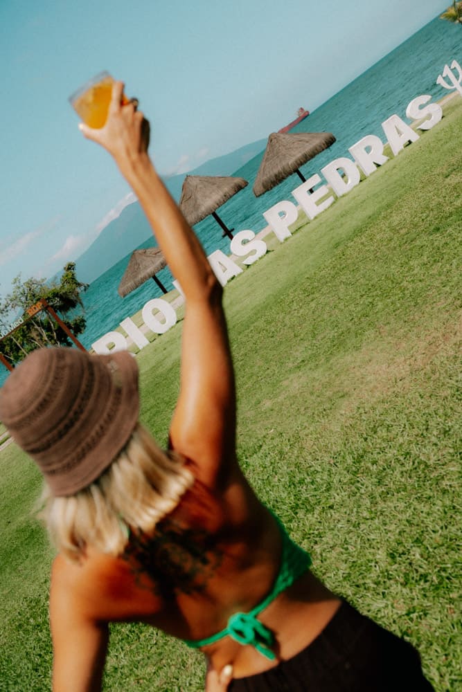 Femme au bob levant son verre devant le panneau Rio das Pedras, vacances lifestyle au Club Med