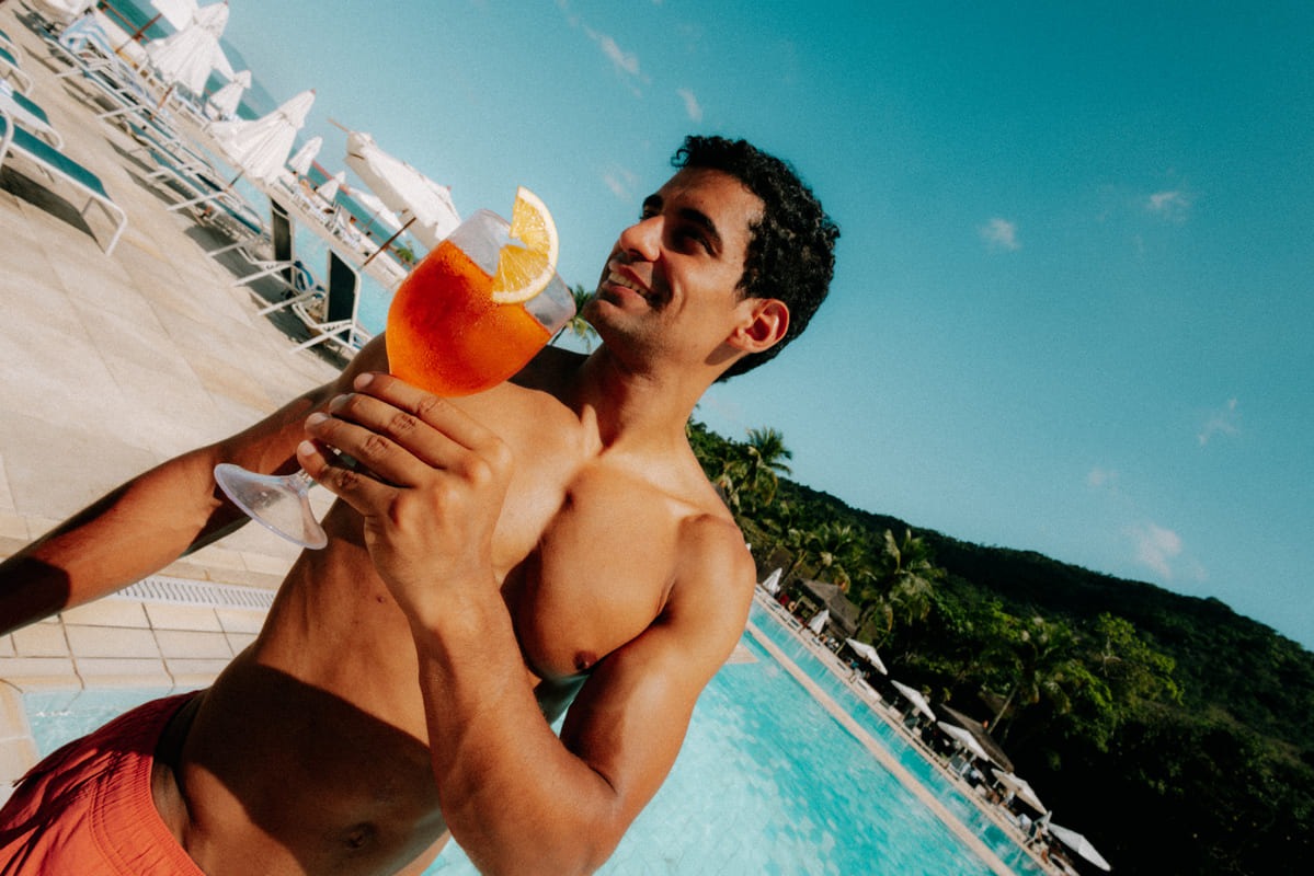 Homme souriant tenant un spritz au bord de la piscine en contre-plongée, Club Med Rio das Pedras