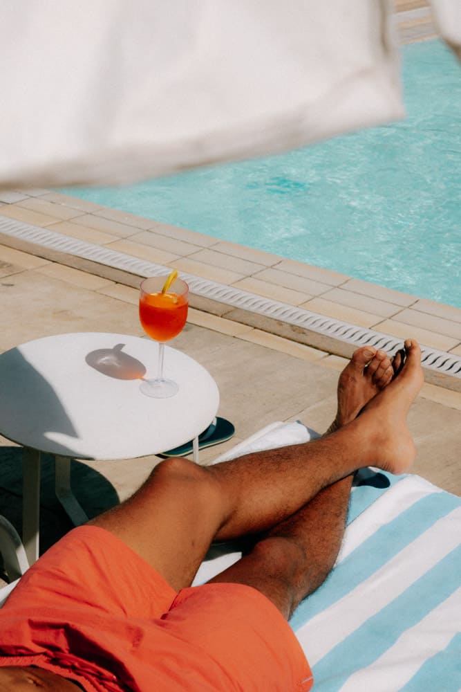 Spritz posé sur une table blanche à côté d'un transat rayé, bord de piscine du Club Med Rio das Pedras