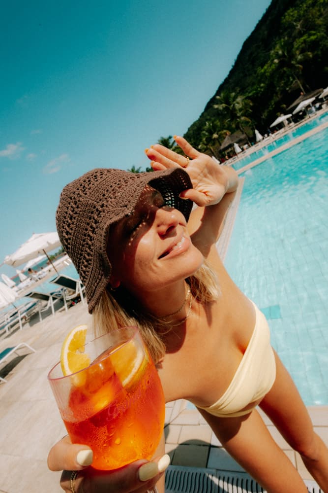 Portrait d'une femme au bob tenant un spritz au soleil, photographie lifestyle Club Med Rio das Pedras