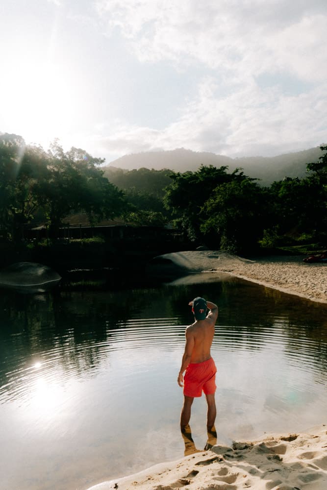 Homme en short rouge de dos dans la rivière au coucher du soleil, reflets des montagnes, Club Med Rio das Pedras