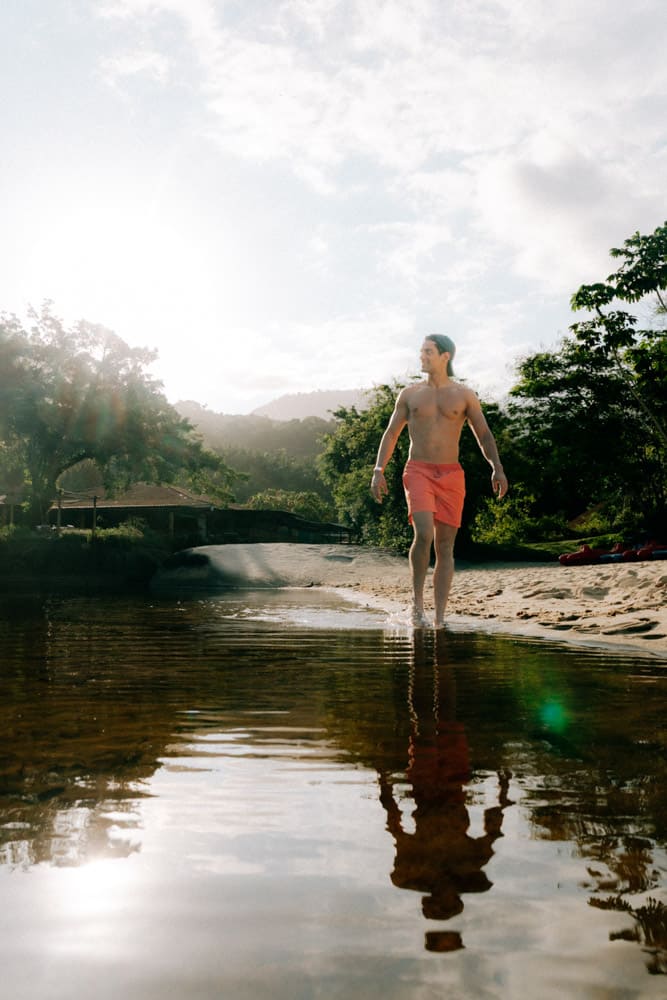 Homme en short rouge marchant dans la rivière en contre-jour, golden hour au Club Med Rio das Pedras