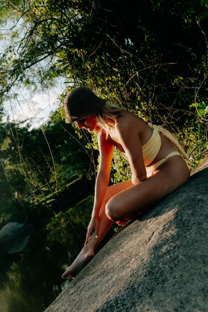 Femme en maillot jaune assise sur un rocher au bord de la rivière, lumière dorée, Club Med Rio das Pedras